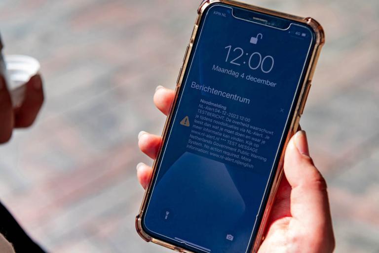 Hand met iPhone scherm waarop een NL-alert zichtbaar is