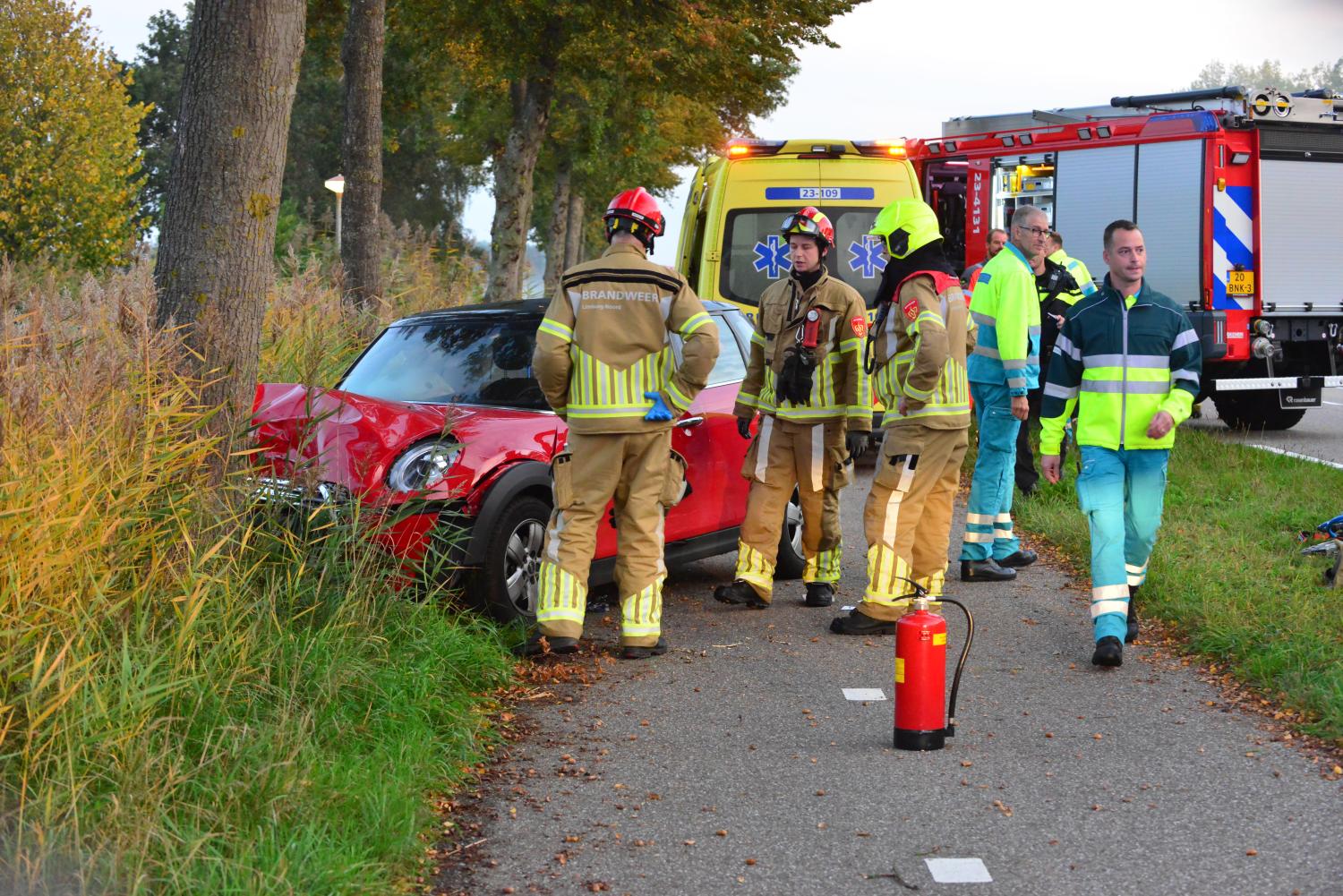 Auto tegen boom, hulpverleners die helpen